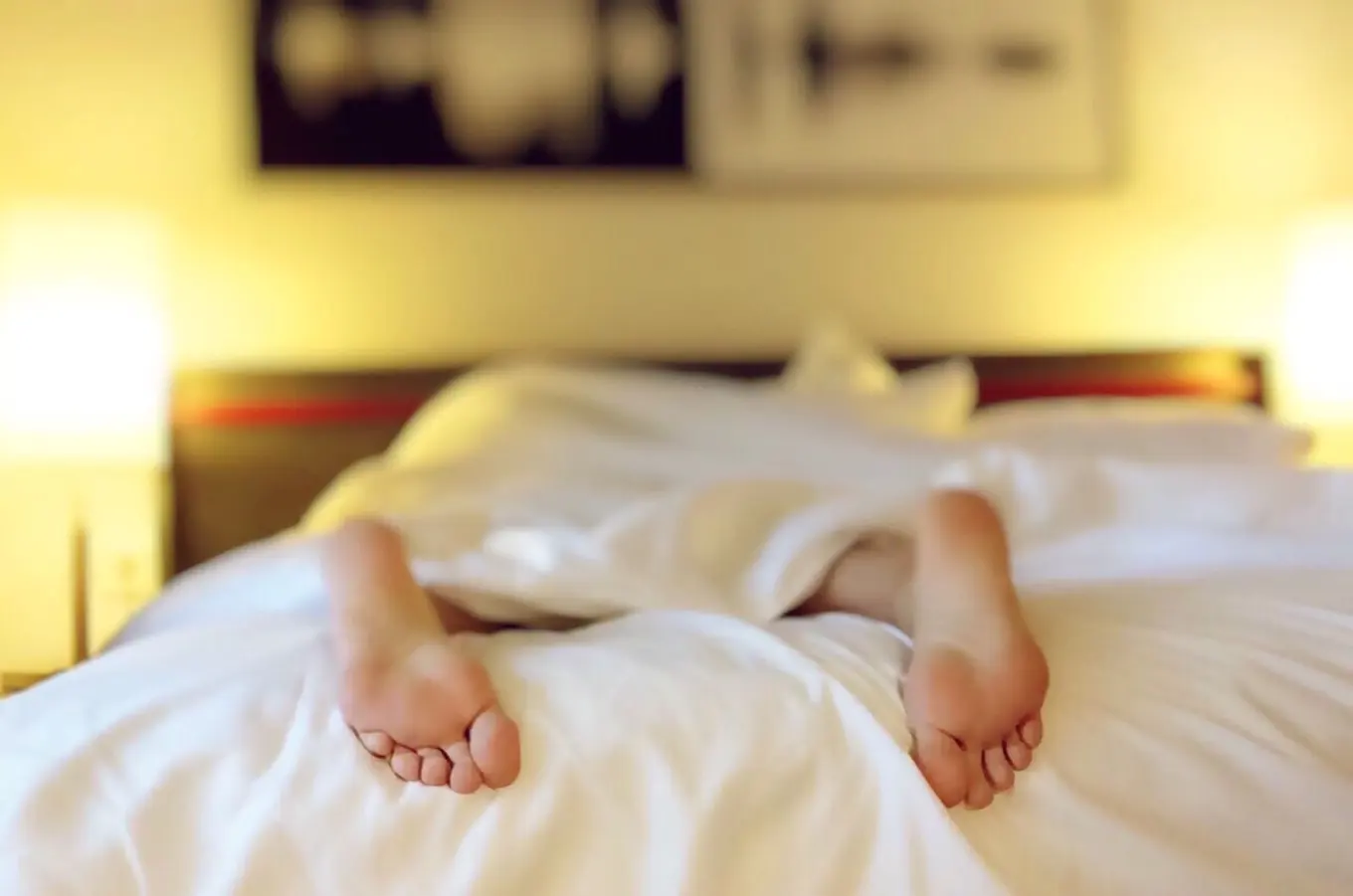 Two bare feet sticking out from under a white duvet.