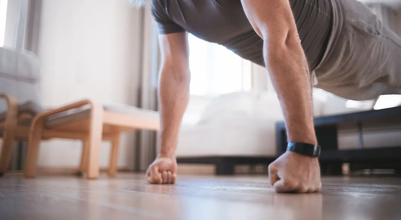 A man doing knuckle push-ups on a living room floor, his head out of frame.