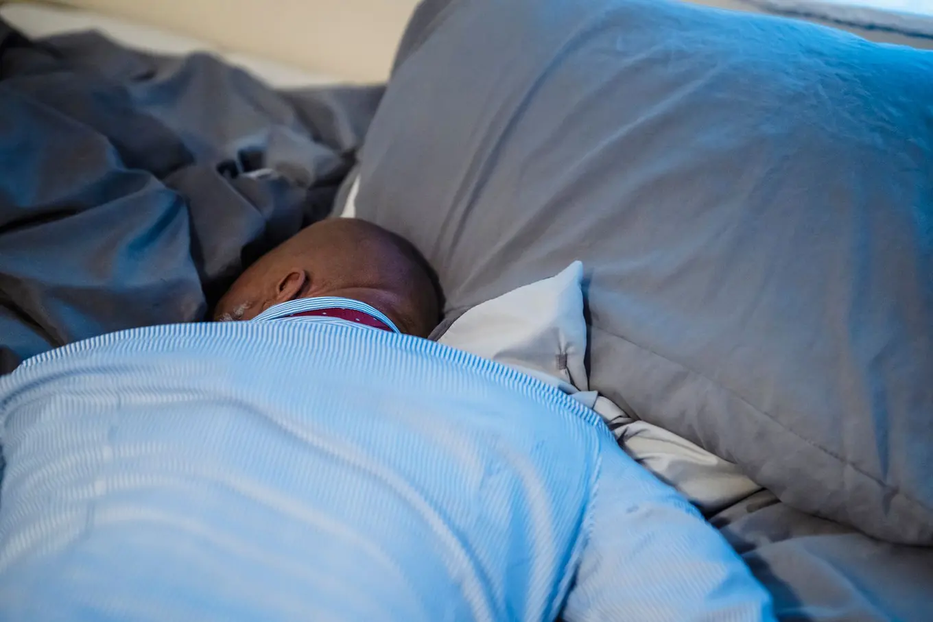 A person asleep face down in a pillow under a blue duvet.