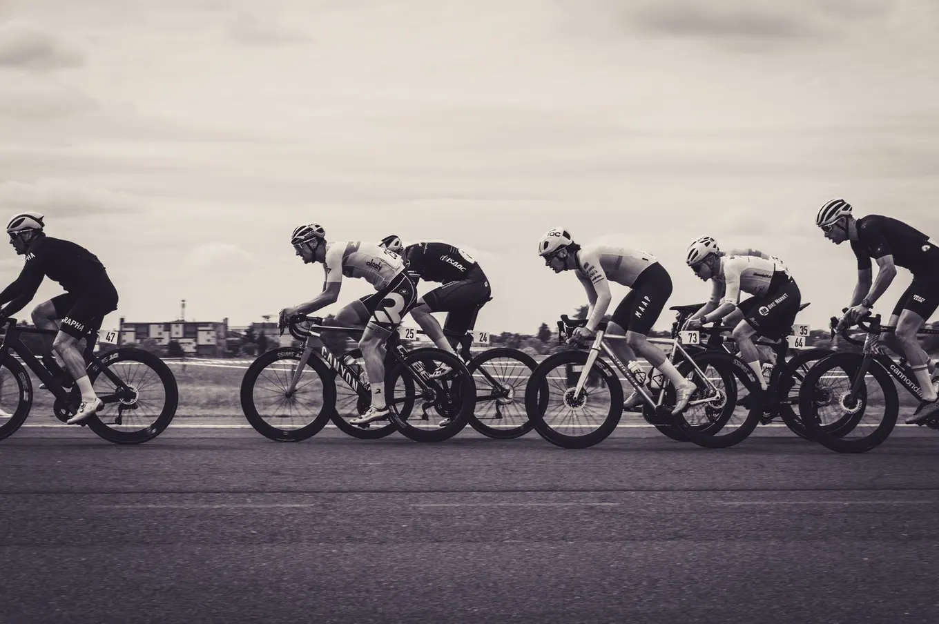 Black and white photo of a line of road cyclists racing side by side.